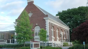 Nestled amidst the trees, this red brick building features large arched windows and white trim, creating a picturesque stop on the Columbia City Tour in Seattle.