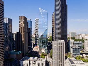 Skyline view of a city with modern skyscrapers, including a prominent glass tower with a triangular peak, surrounded by other tall buildings under a clear blue sky—experience this breathtaking scene on a Seattle Skyline Tour.