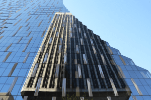 Experience the "Through The Looking Glass Tour" with this architectural close-up of a modern glass skyscraper, its reflective facade shimmering under a clear blue sky.
