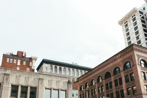 Cityscape with vintage brick and stone buildings under a cloudy sky. From Skid Row to Skyscrapers, prominent structures include the Hartford Building and other early 20th-century architectural styles.