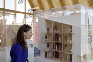 A woman with brown hair and a blue top closely inspects one of the Danish Housing Lab models 