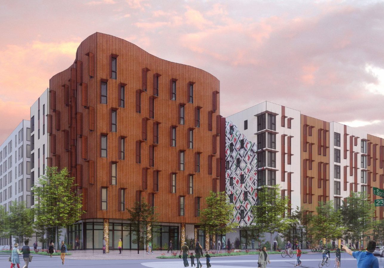 A digital rendering of the final concept for the Africatown Plaza building. The left side of the building features an undulating facade with a rusted steel exterior. The right side of the building is rectangular with long vertical windows and a mural. There is a community plaza in front of the building.