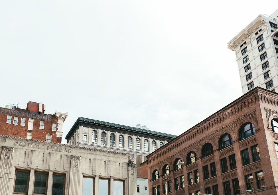 Cityscape with vintage brick and stone buildings under a cloudy sky. From Skid Row to Skyscrapers, prominent structures include the Hartford Building and other early 20th-century architectural styles.