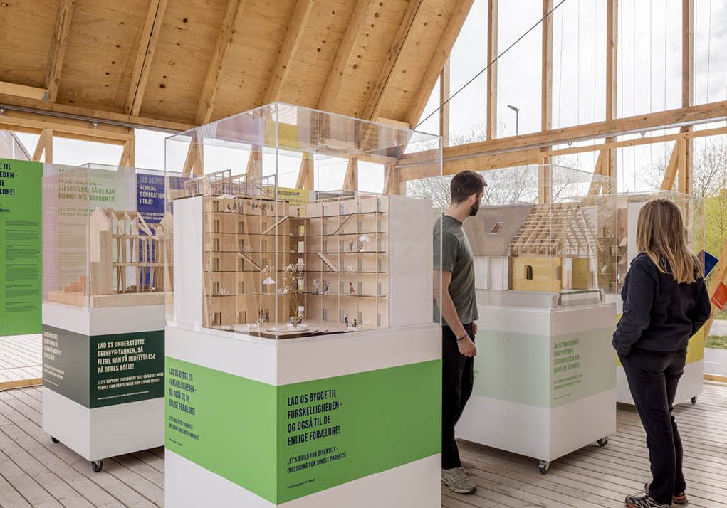 Two adults view architectural models on white platforms.